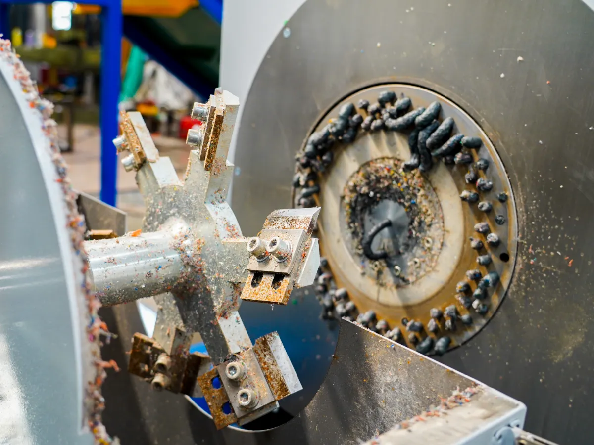 a close-up view of a plastic granulator or shredder, focusing on the cutting chamber where the rotating blades are visible. These blades are instrumental in breaking down plastic into smaller pieces as part of the recycling process. The granulator's blades have plastic residue on them, suggesting that the machine has been actively used to process materials. The presence of rust and wear on the components indicates that the machine may be well-utilized or in need of maintenance to ensure optimal performance. The design of the rotor and the positioning of the blades are crucial for the efficiency and effectiveness of the granulation process. Proper maintenance, including regular cleaning and sharpening of the blades, is essential to keep the machine running smoothly and to prevent contamination of the recycled material.