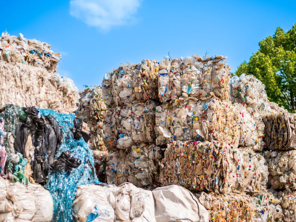 velike bale komprimiranog plastičnog otpada, koje se obično pripremaju za recikliranje. Ove bale se formiraju nakon procesa sortiranja i čišćenja, gdje se različite vrste plastike komprimiraju u upravljive blokove za lakši transport i daljnju obradu. Raznolikost boja unutar svake bale ukazuje na mješavinu različitih plastičnih predmeta, što sugerira da bi te bale mogle biti namijenjene objektu koji će dalje sortirati i reciklirati materijal u nove plastične proizvode. Ovo je uobičajena praksa u industriji recikliranja kako bi se smanjio volumen otpada, što transport materijala do postrojenja za recikliranje čini isplativijim. Postrojenja za reciklažu često koriste balirke za zbijanje sortiranih materijala koji se mogu reciklirati u guste, vezane bale. Bale štede prostor tijekom skladištenja i transporta, a njihov ujednačen oblik olakšava rukovanje i obradu