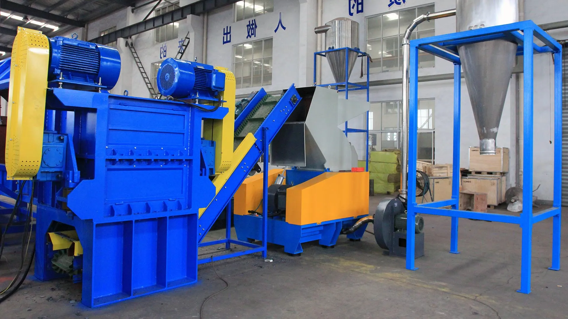 an image of a rigid plastic granulator machine setup in a factory. These machines are designed for size reduction of large volumes of plastic, which is an essential process in recycling facilities to manage and recycle plastic waste effectively. The image shows various parts including the conveyor system that feeds plastic into the granulator, the granulator itself which grinds the plastic into smaller pieces, and the collection system that gathers the processed material.