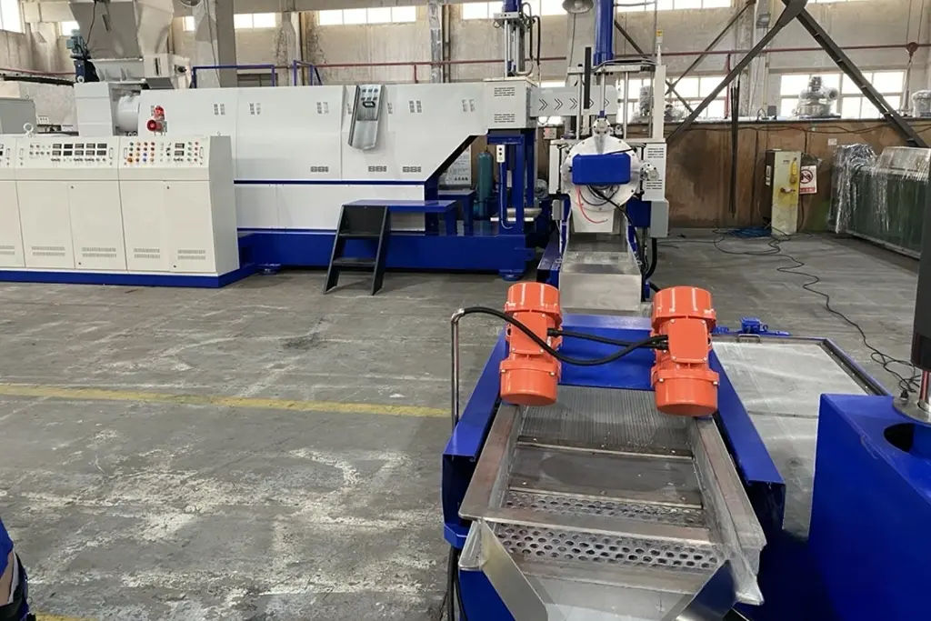 Industrial plastic recycling machine in a factory, featuring conveyor and processing unit.